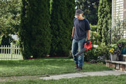 Photo of a person using a red Craftsman cordless leaf blower, SKU CMCBL710B, on a grassy lawn near shrubs.