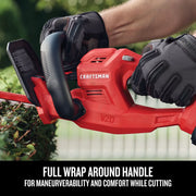 Photo of CRAFTSMAN hedge trimmer CMCHT810B with gloves, red body, wraparound handle trimming a bush.