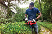 Person trimming hedges outdoors with CRAFTSMAN hedge trimmer, SKU CMCHTS820B, in a garden setting.