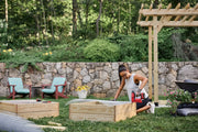 Photo of person using CRAFTSMAN CMCN410B cordless nailer to assemble wooden garden box outdoors, with garden tools nearby.
