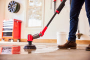 Photo of CRAFTSMAN CMCPSHB power scrubber in use cleaning a wet garage floor, close-up angle showing lower handle and brush.