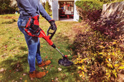 Photo of Craftsman CMCST900D1 cordless string trimmer in use trimming grass near bushes in a garden.