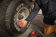 Photo of person using CRAFTSMAN CMMT14134 digital tire gauge on large vehicle tire in garage setting.