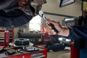 Photo of CRAFTSMAN ratchet wrench SKU CMMT86324V used to loosen bolt on vehicle in automotive workshop.