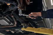 Photo of a person using a CRAFTSMAN ratchet wrench, SKU CMMT86334V, on a car undercarriage in a workshop.