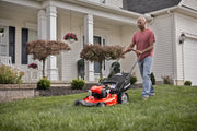 Photo of a person using a Craftsman lawn mower CMXGMAM221101 on a grassy yard in front of a house.