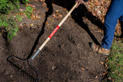 Photo of Craftsman garden rake SKU CMXMLTP35315 with wooden handle and metal tines in use on soil outdoors.