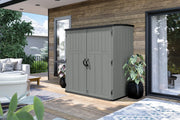 Photo of Craftsman storage shed SKU CMXRCSCBMSC6252 in gray on patio beside wooden wall and potted plants.